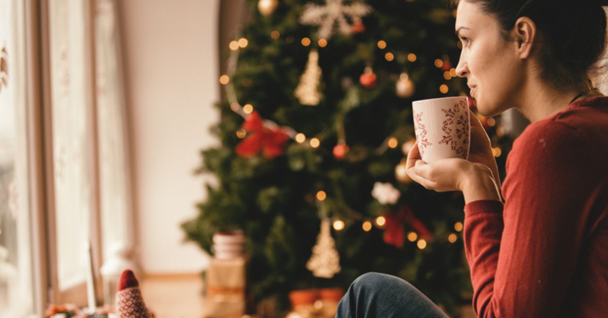 woman sipping coffee, looking out window at Christmas