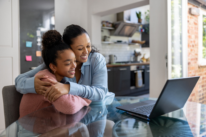 mother hugging college-aged daughter while looking at a laptop